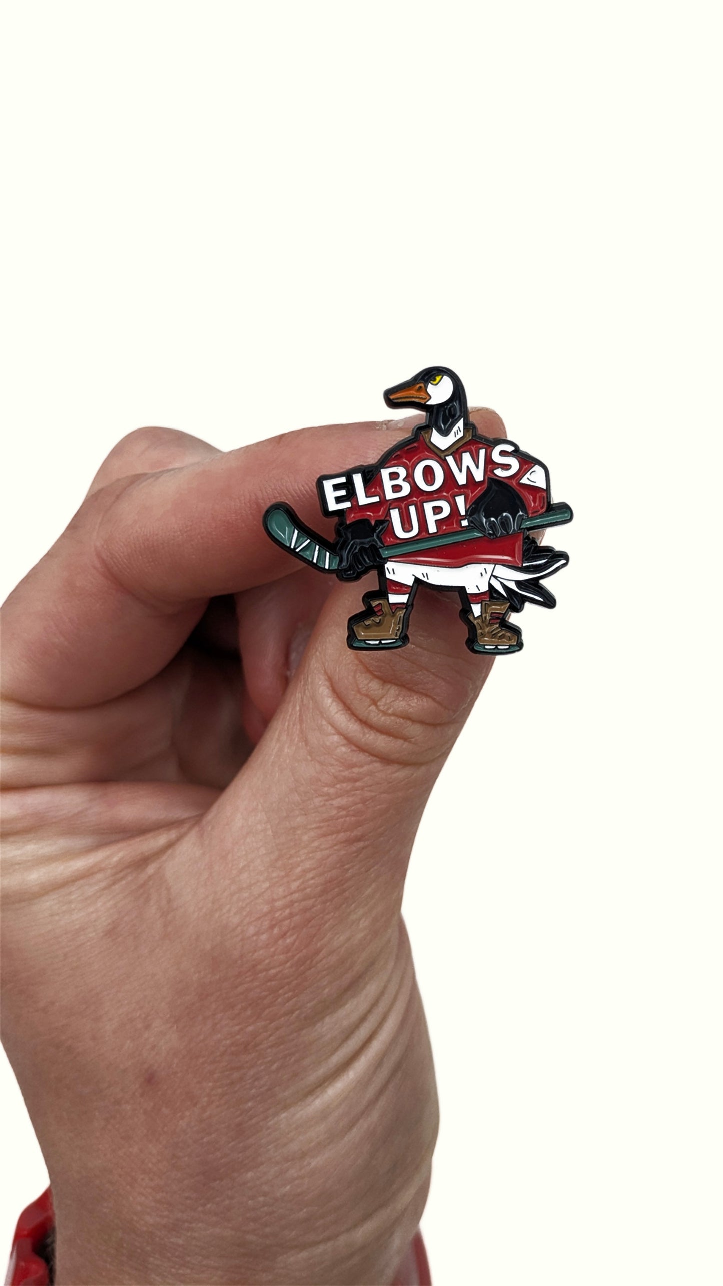Enamel pin of a Canada goose in a red hockey jersey holding a stick with the words "Elbows Up!" in hand
