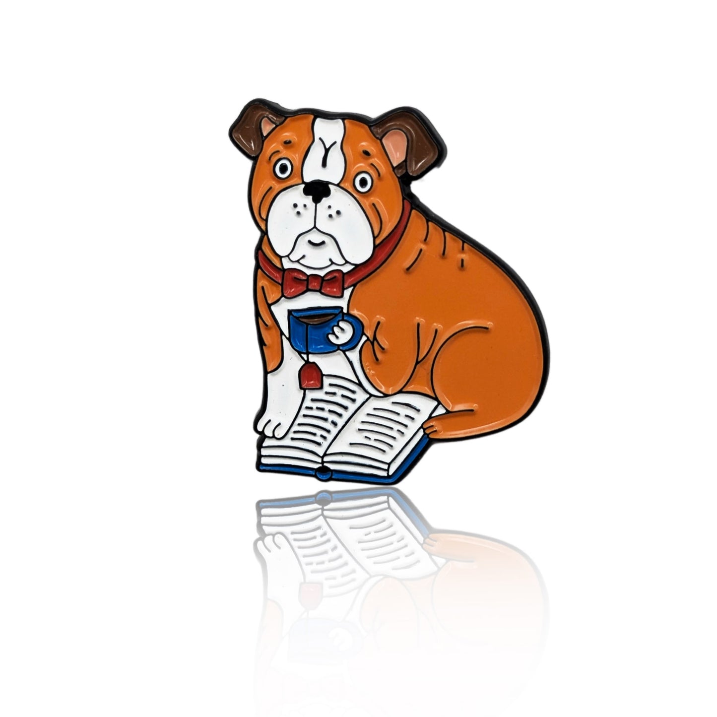 Enamel pin of a cartoon Bulldog with a bowtie, holding a teacup and sitting on an open book