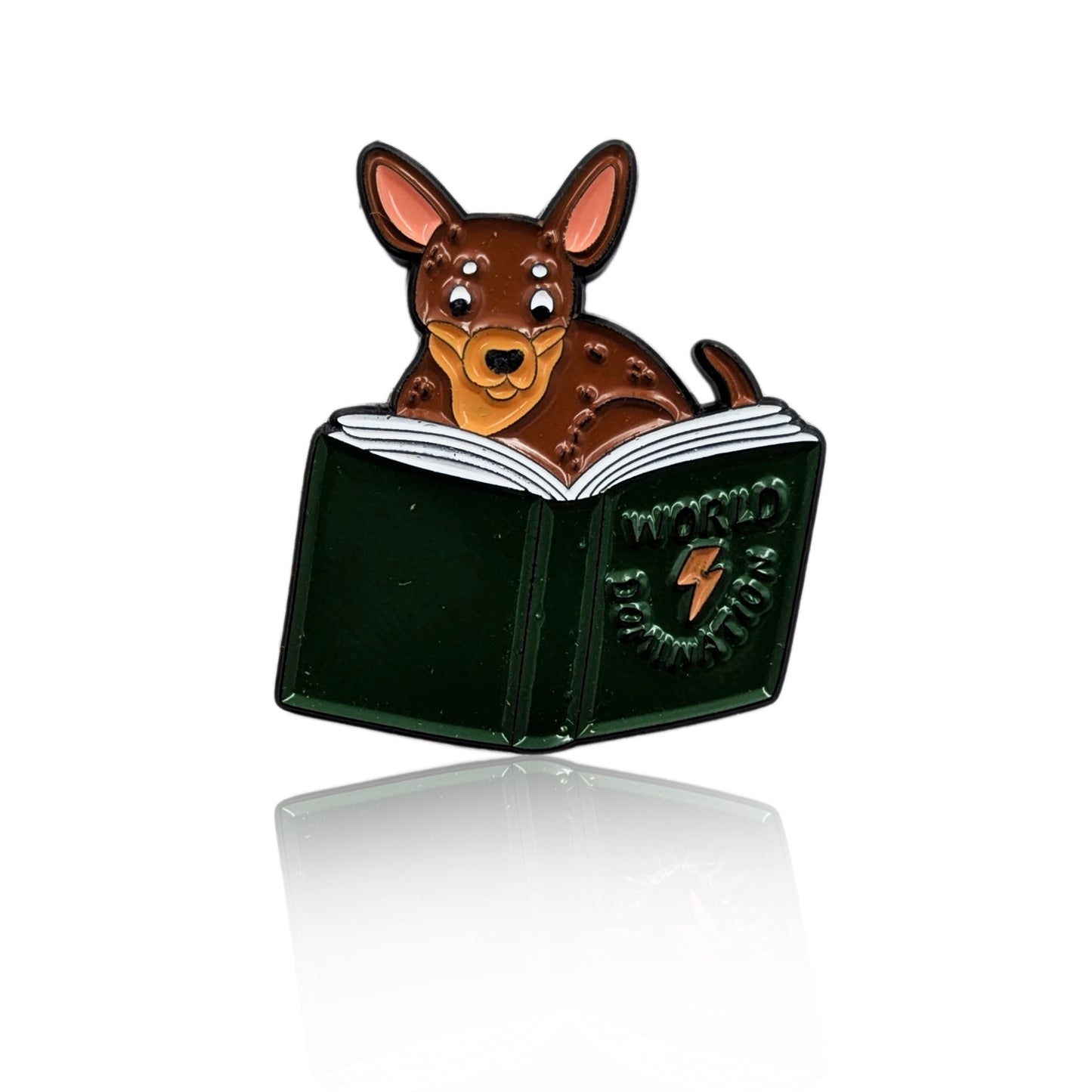 Enamel pin of a cartoon Chihuahua reading a book titled “World Domination”