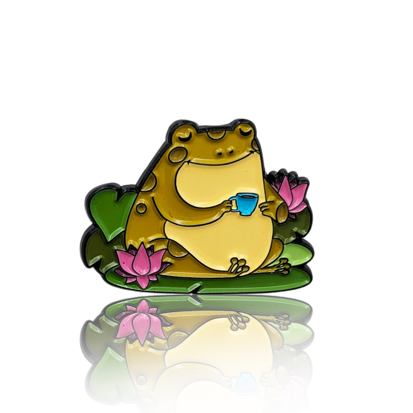Enamel pin of a chubby toad holding a blue teacup, surrounded by pink lotus flowers and lily pads