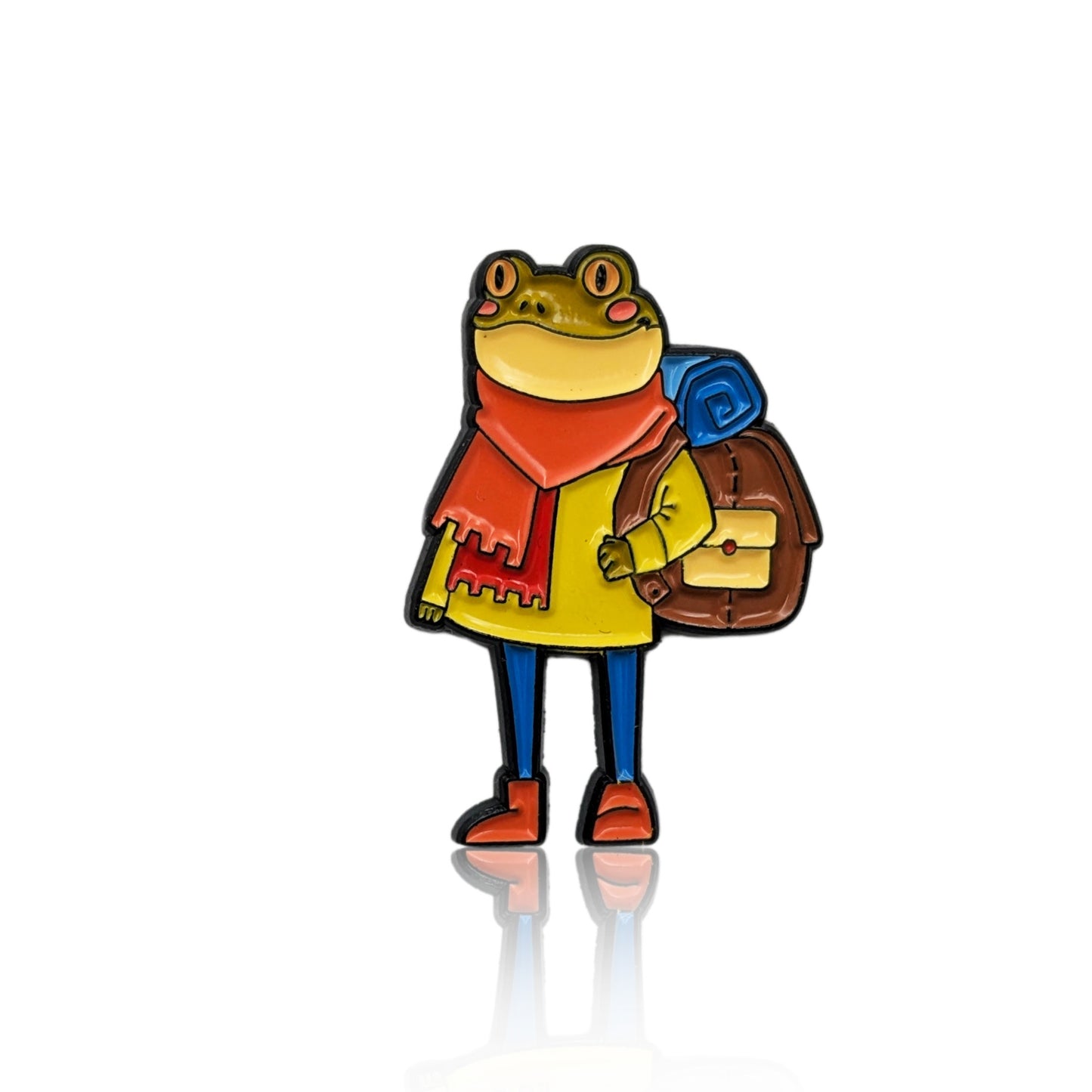 Enamel pin of a frog wearing a yellow coat, red scarf, and backpack with a rolled-up mat