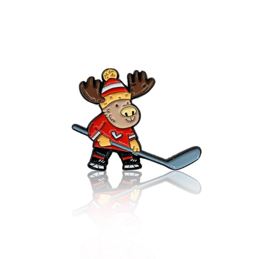 Enamel pin featuring a cartoon moose playing hockey, dressed in a red jersey with a heart emblem and a cozy winter hat. The moose holds a hockey stick, ready for action, making it a perfect accessory for hockey lovers and Canadian pride enthusiasts. The pin has a glossy finish with a reflection on a white background.