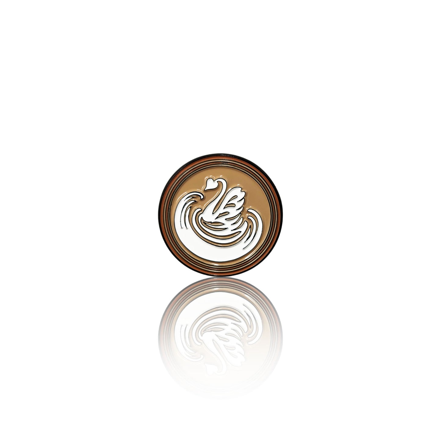 Round enamel pin on a white background with a coffee base and white swan-shaped latte art design, shown with its reflection below.
