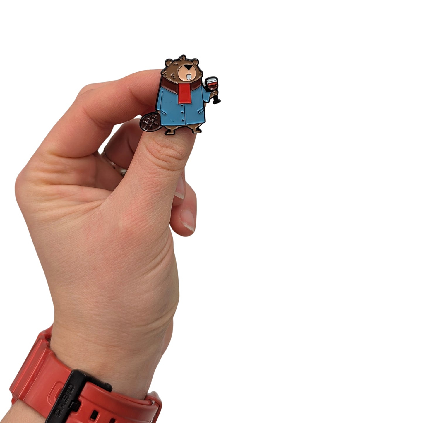 Beaver enamel pin held in hand, showing a dressed beaver wearing a blue coat and red scarf while holding a glass of wine
