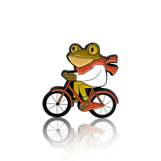 Enamel pin of a frog riding a red bicycle with a red scarf blowing in the wind
