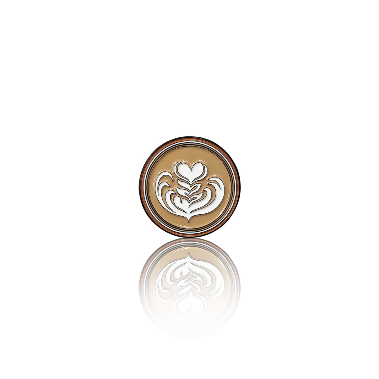 Round enamel pin on a white background with a creamy coffee base and a white latte art heart design, shown with its reflection.