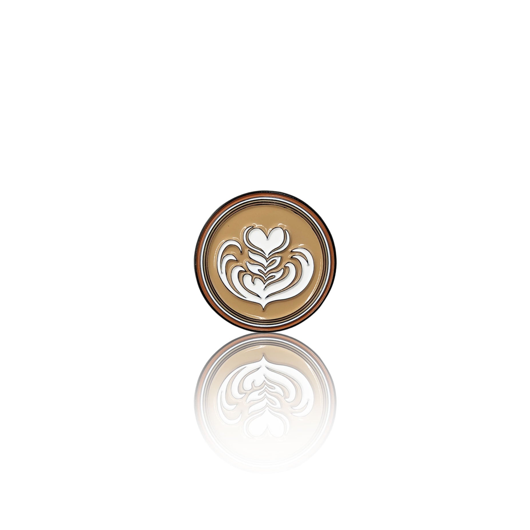 Round enamel pin on a white background with a creamy coffee base and a white latte art heart design, shown with its reflection.
