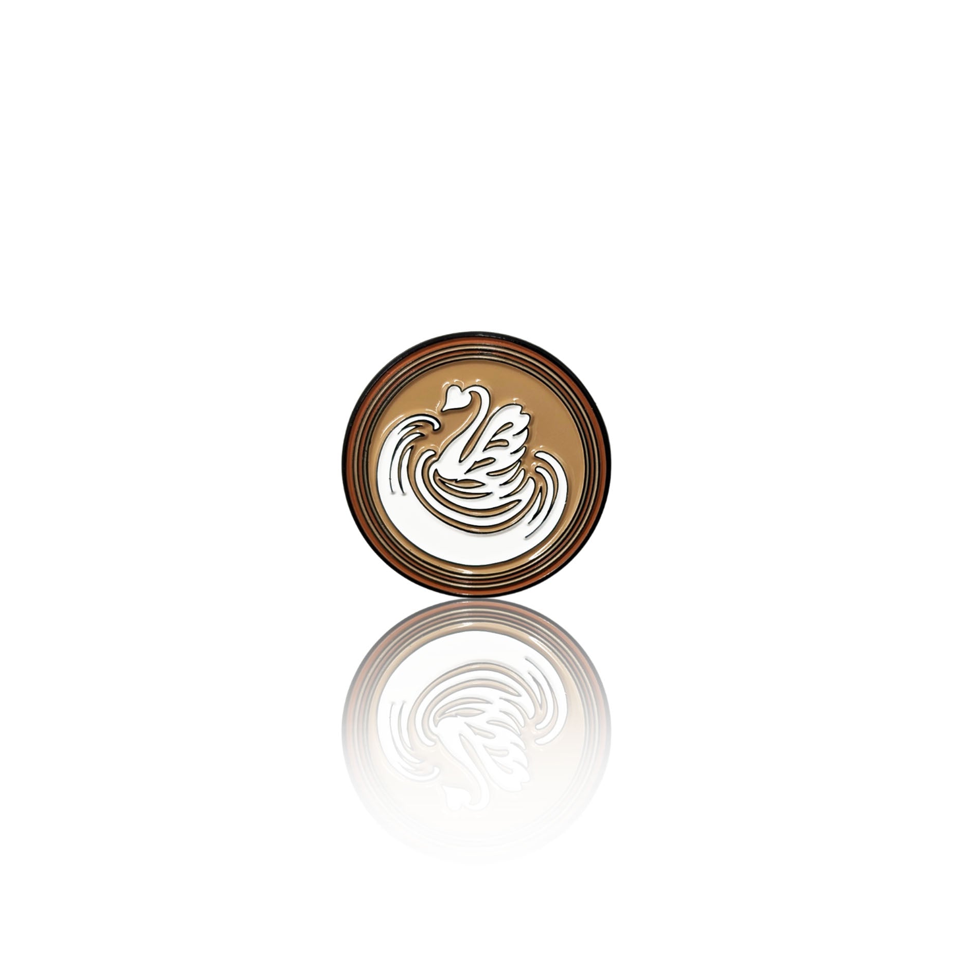 Round enamel pin on a white background with a coffee base and white swan-shaped latte art design, shown with its reflection below.