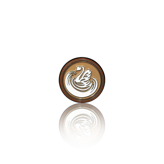Round enamel pin on a white background with a coffee base and white swan-shaped latte art design, shown with its reflection below.