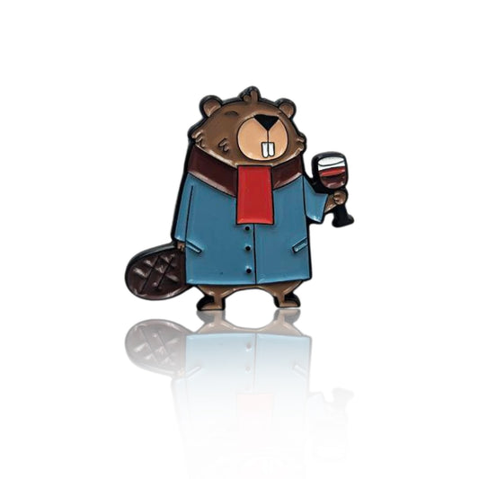 Enamel pin of a beaver wearing a blue coat and red scarf, holding a glass of red wine, shown on a clean white background