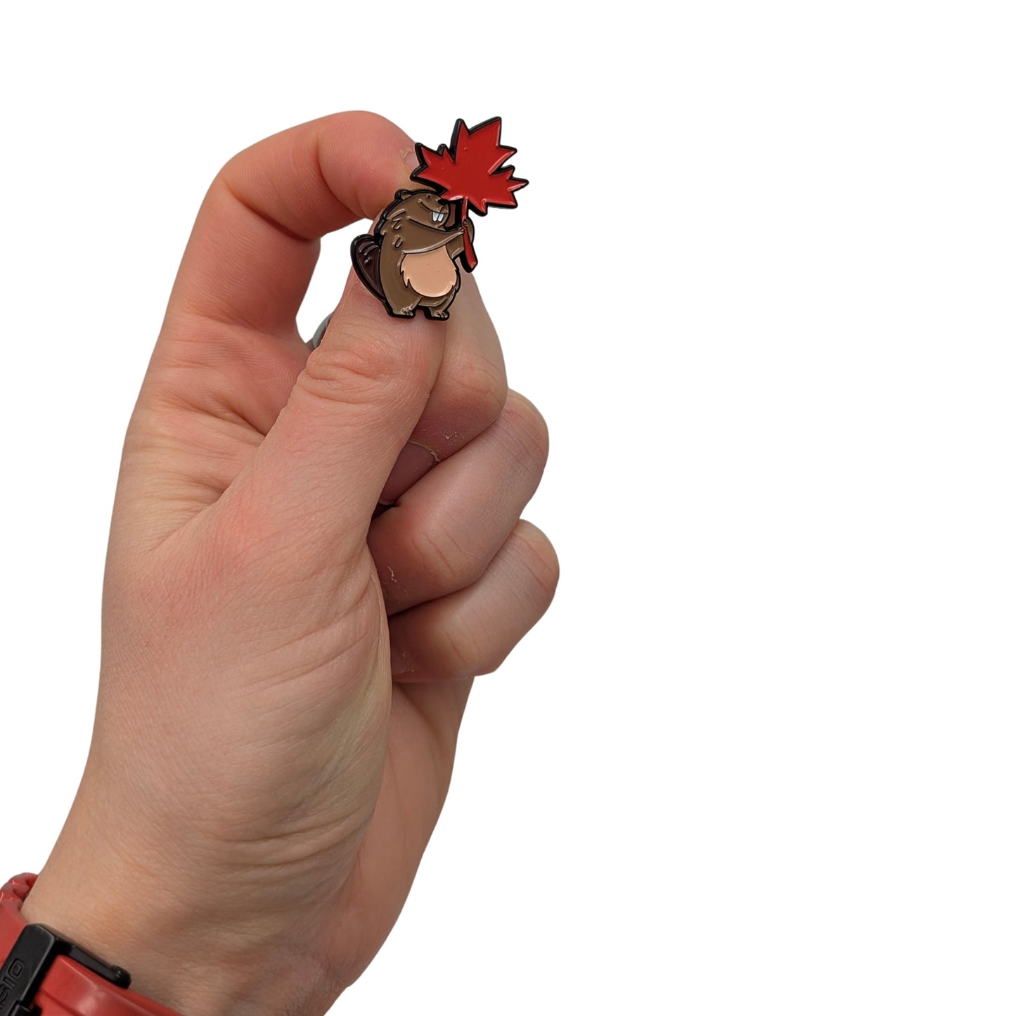 Beaver enamel pin holding a red maple leaf, shown in hand, featuring a cute cartoon beaver design