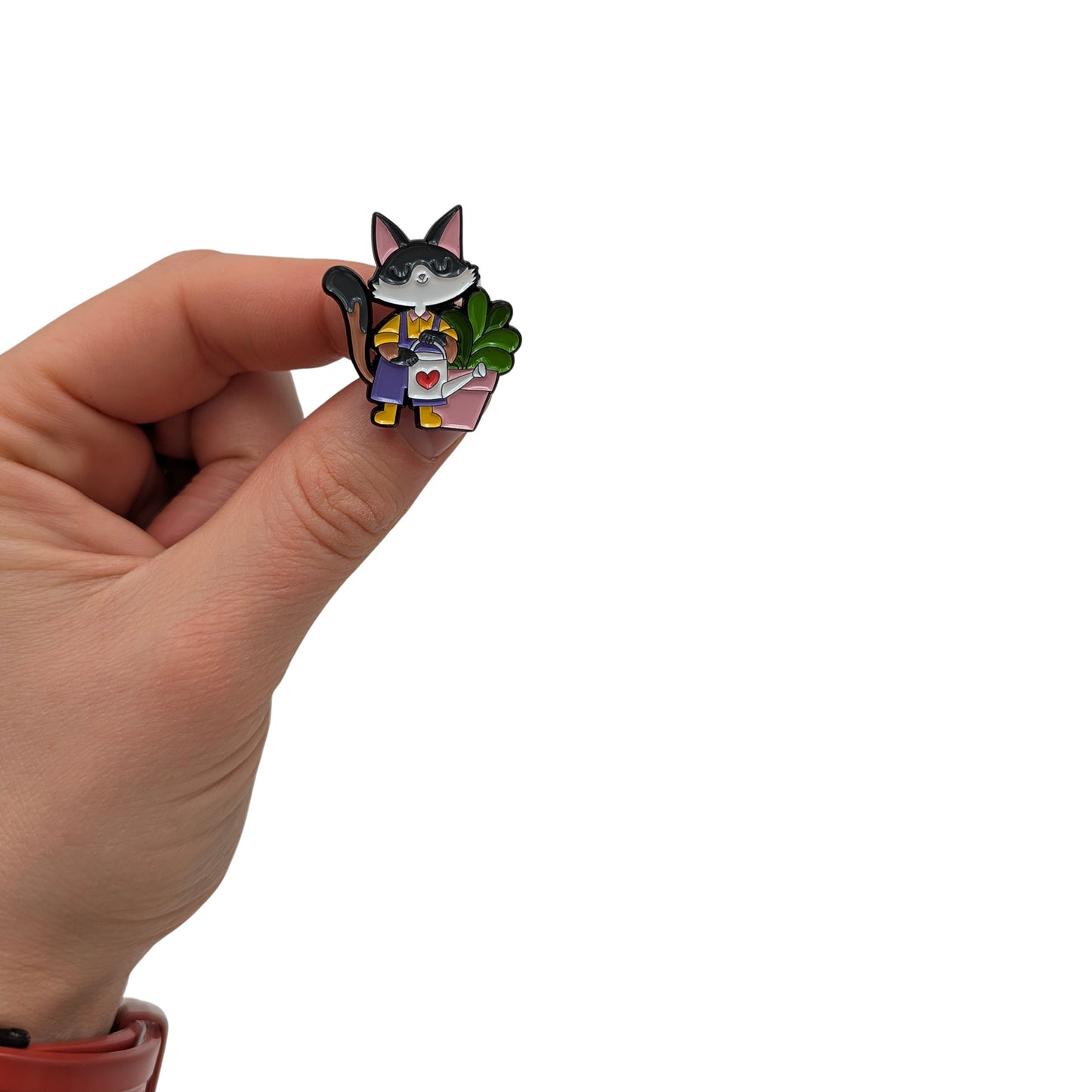 Cat enamel pin held in hand, wearing gardening clothes and holding a watering can next to a potted plant