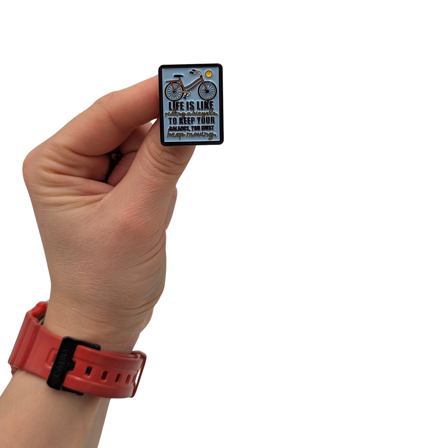 Inspirational enamel pin with a bicycle and motivational quote, shown held in hand