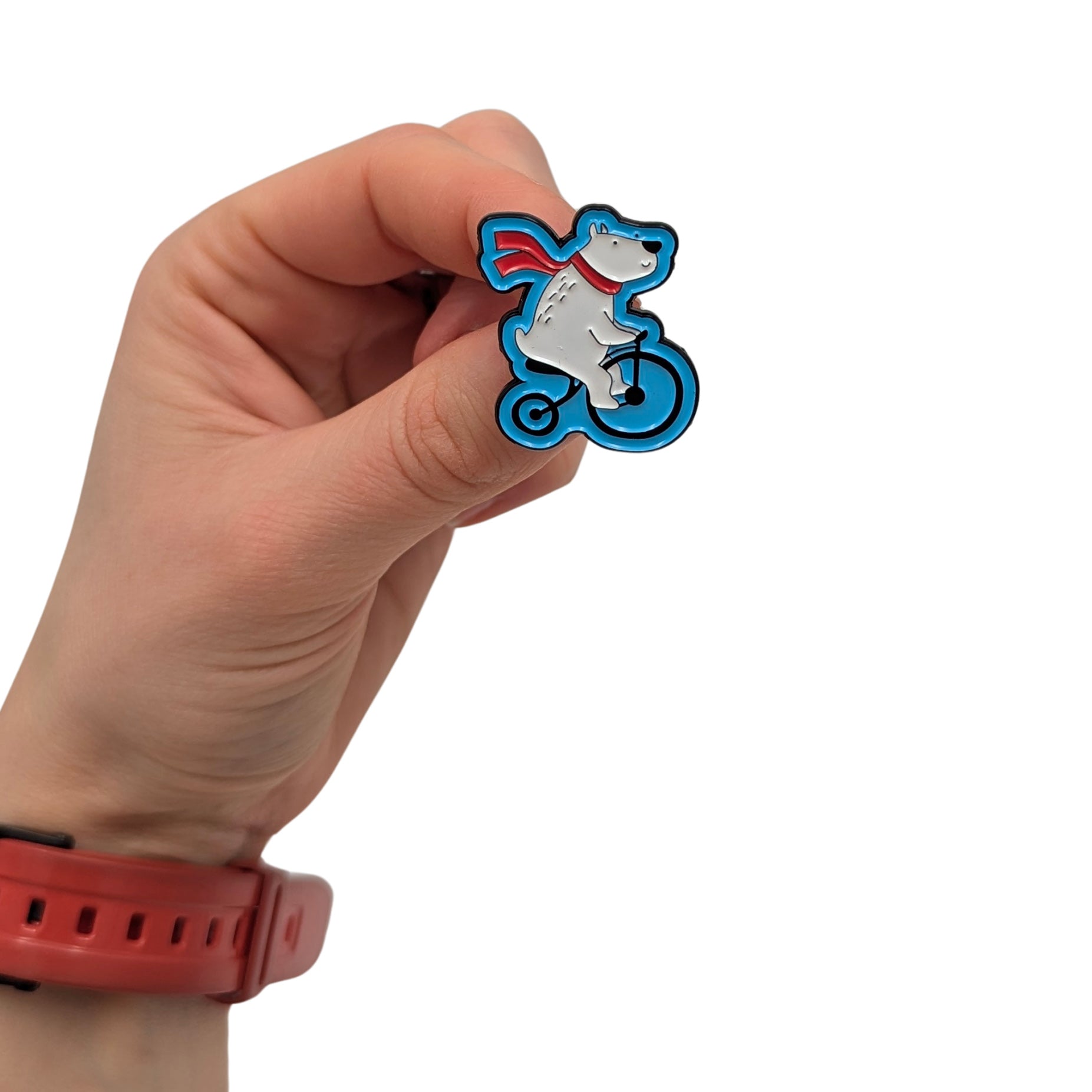 Polar Pedal Pete enamel pin held in hand, featuring a polar bear riding a bicycle with a red scarf