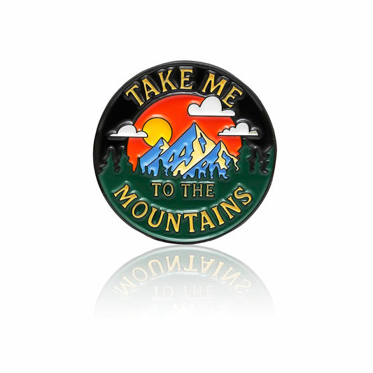 Mountain enamel pin with sunset, trees, clouds, and text “Take Me to the Mountains,” 32mm by PINBOX
