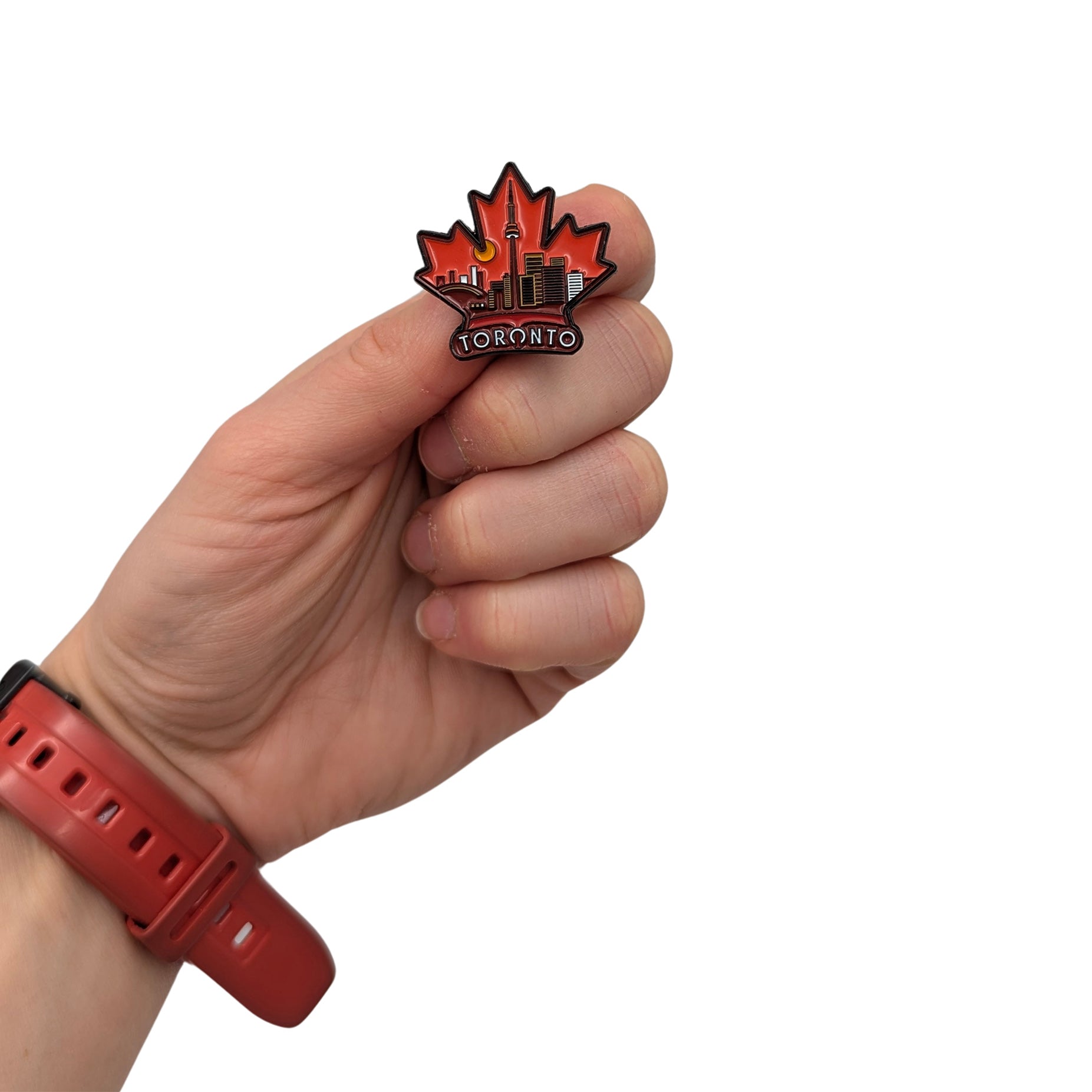 Toronto maple leaf enamel pin held in hand, showing a red leaf shape with city skyline and CN Tower