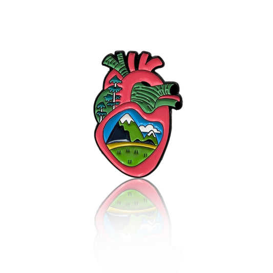 Wild at Heart enamel pin showing an anatomical heart with mountains, trees, and landscape inside on white background